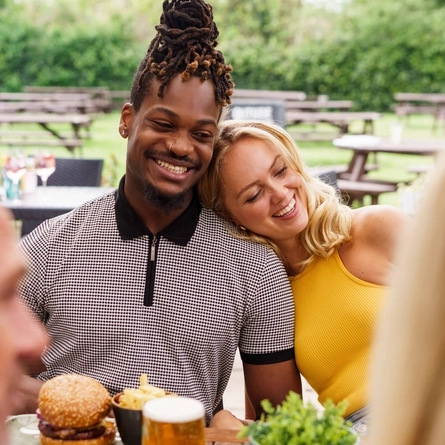 An exterior shot of people enjoying drinks and burgers within the beer garden seating area at a Community Pub with Food venue.