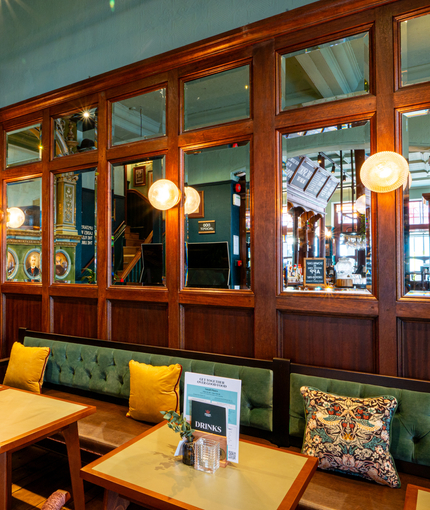 The interior restaurant seating area of The Fountains Abbey, with upholstered booth seating, wooden tables, a fireplace, and a wood panelled wall inlaid with mirrors.