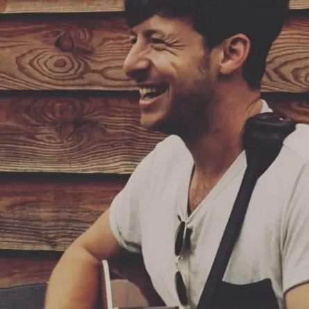 A man playing a guitar and smiling.
