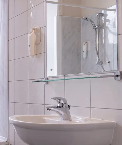 The interior hotel bathroom with a sink, mirror and bath with a shower over the bath at the Brentwood.