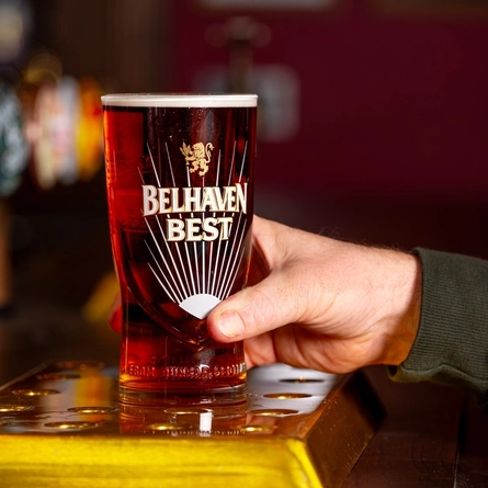 A close up view of a hand picking up a glass of Belhaven Best which sits on a golden drinks tray on the bar.