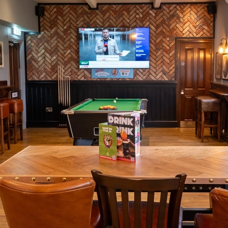 The interior games area at The Hussey Arms, with a pool table, a TV on the patterned brick wall, and restaurant seating.