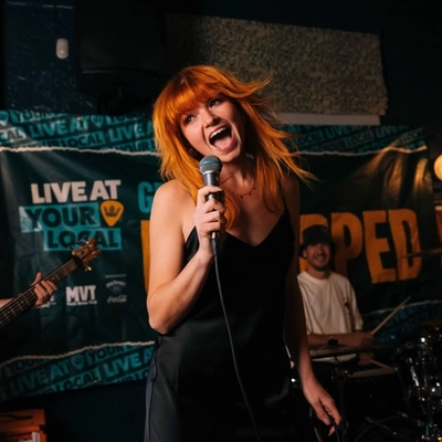 A lifestyle image showing a live band performing on a stage within the interior of a Greene King venue.