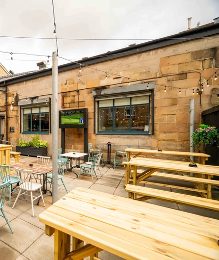 The exterior beer garden and seating area with benches and tables and chairs and also two TV's on the walls at the Armstrongs.