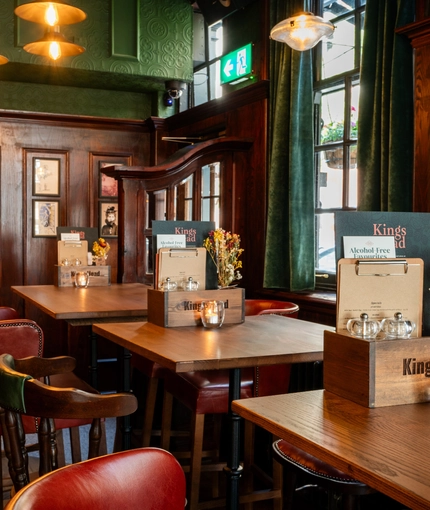 An interior restaurant seating area at the King's Head, with green velvet curtains; dark wood panelled walls; and upholstered chairs.