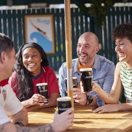 A mixed group of people seated at an outdoor table holding drinks.