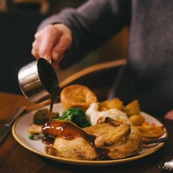 A close up image of gravy being poured over a plated Sunday Roast dish sat on a table within the interior restaurant seating area at an Urban Core Venue.