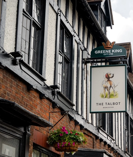 A close up view of the pub sign hanging on the exterior wall of The Talbot. The sign features an illustration of a dog standing on grass above the words "The Talbot, Worcester", on a white background.
