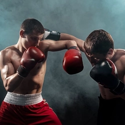 Two people wearing shorts and boxing gloves, boxing each other, surrounded by smoke or fog.