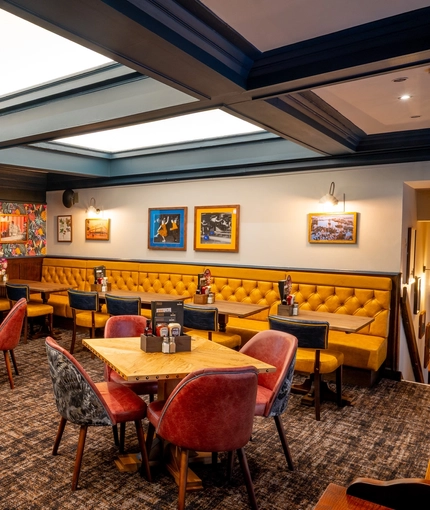 An interior restaurant seating area at the Old School House in Aberdeen, with upholstered chairs and booth seating, wood panelling and a TV on the wall, and large, square sky lights in the ceiling.