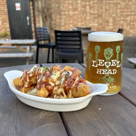 Food in a roasting dish and a pint of Level Head on an outside table.