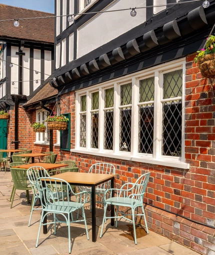 The exterior facade and seating area at The Walkford, with flower baskets hanging on the walls, and string lights above the tables and chairs.