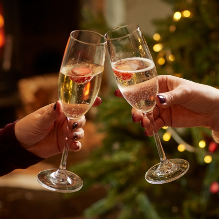 A product image of 2 glasses of white sparkling wine celebrating with a cheers within the interior of a Chef & Brewer venue.