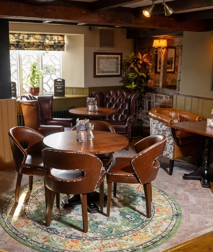 The interior restaurant seating area of The Blue Cap in Sandiway, with upholstered chairs, patterned brick flooring, and wooden beams on the ceiling. 
