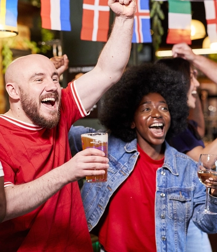 A mixed group of people holding a drink and cheering.