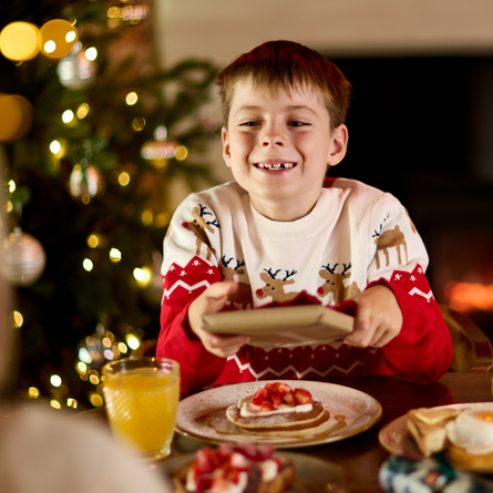 An image of an adult and child exchanging a gift while enjoying fruit juice and dishes from the Breakfast with Santa menu at Chef & Brewer venues.