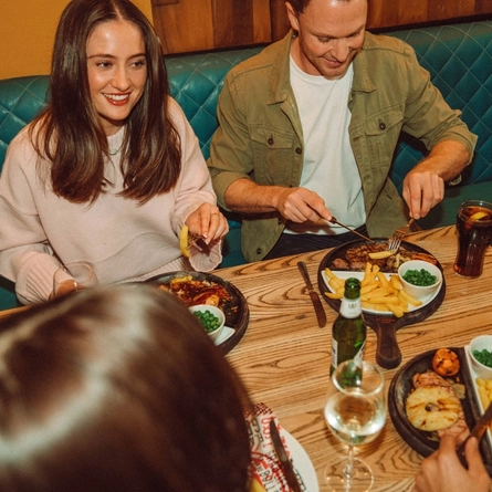 An image showing a group of people sat around a table enjoying mains dishes and drinks at a Flaming Grill venue.