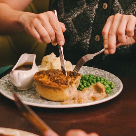 An image of a group of friends sat at a table enjoying festive main dishes and various drinks within the interior restaurant seating area at a Proper Local venue.