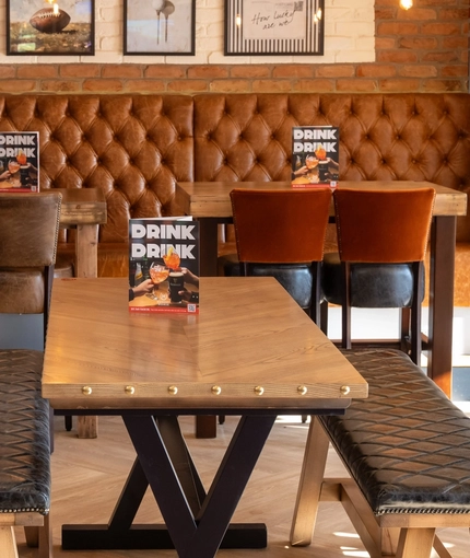 An interior restaurant seating area at The Weathervane, with upholstered chairs, benches, and booth seats, and framed artwork on the wall.