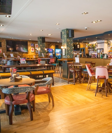 The bar and interior restaurant seating area of The Merlin, with wooden tables and bench seating, TVs on the walls, and pub game machines.