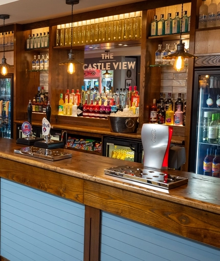 The interior bar with hanging pendant lighting, venue branding on a mirror behind the bar and tiled flooring at The Castle View.