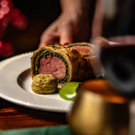 A close up lifestyle image showing a plated Christmas/Festive main dish being placed down on a table within the interior restaurant seating area.