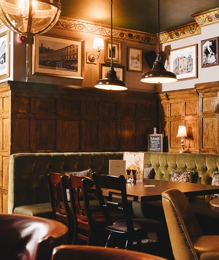 The wood panelled interior restaurant seating area at the Masons Arms in Mayfair, with a fireplace, an upholstered booth corner seat, and flowers carved into the coving.