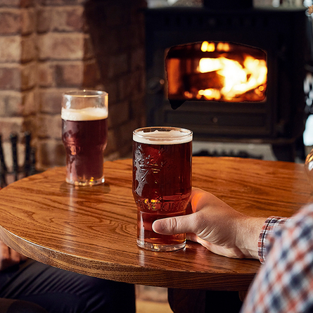 Two pints of beer sitting on a wooden table of a pub