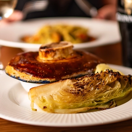 An advertising image showing a plated pie dish sat on a table with a pint of Guinness within the interior restaurant seating area from the AW menu.