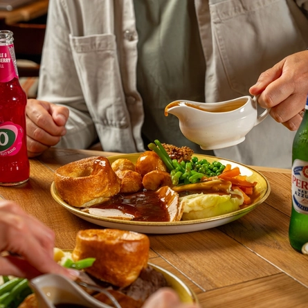An image of gravy being poured over a Sunday Roast with various drinks within the interior restaurant and seating area at a Hungry Horse venue.