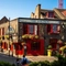 The exterior facade, signage, and seating area of The Anchor Bankside in Southwark; with bright red window frames; hanging flower baskets on the brick walls; and flower boxes below the upper window sills.