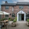 The exterior facade, main entrance, and beer garden seating area at The Malthouse Farm, with wicker chairs, wooden planter boxes, and shade umbrellas.