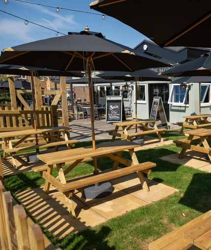 The exterior beer garden seating area with wooden picnic tables and shade umbrellas, at The Man On The Moon in Ipswich.