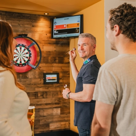 A group of customers in the interior games area playing darts on Fathers Day in a Flaming Grill venue.