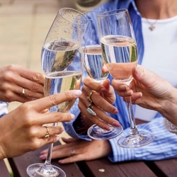A close up image of glasses of Prosecco being held during a Fizz Friday Offer within an exterior beer garden seating area.