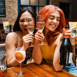 Two girls posing with a bottle and glasses of prosecco.