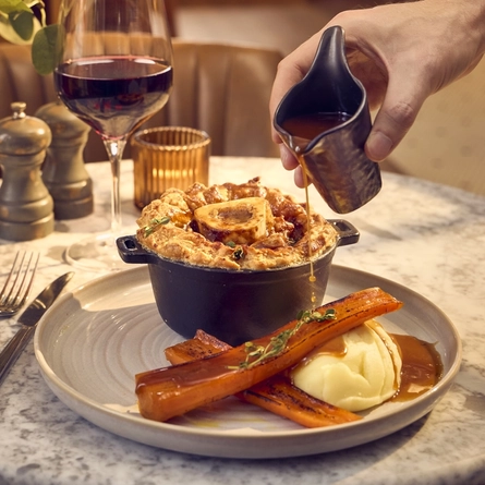 An image of gravy being poured over a plated Slow Braised Short Rib Pie dish from the Autumn/Winter menu available at The White Horses.