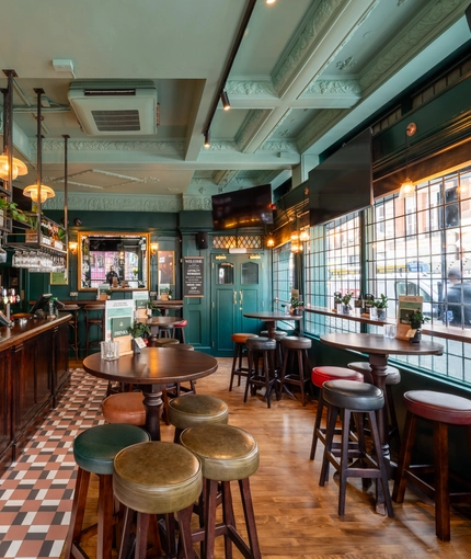 The bar and interior restaurant seating area of The Golden Lion, with TVs on the wall, bar stool seating, and glasses hanging in racks above the counter.