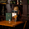 A close up view of menus, salt and pepper mills, a tealight, and a small glass vase filled with dried flowers; on a wooden restaurant table inside The London Apprentice. Books and ornaments stand on wooden shelves next to the table.