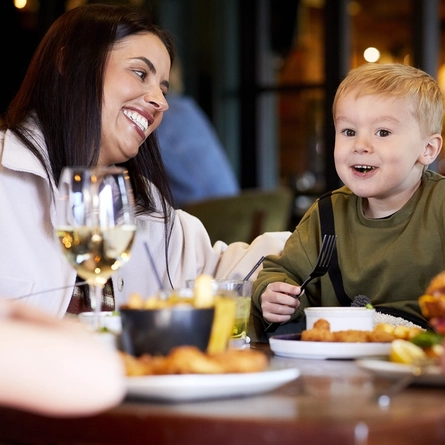 A child and their parent, seated at an indoor table, enjoying food.