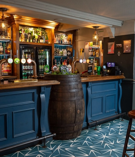 The blue, wood panelled bar inside The Royal Oak in Bishops Cleeve, with a large beer barrel built into the counter.