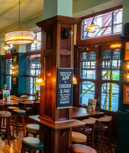 The bar and interior restaurant seating area of The Fountains Abbey, with wooden and metal tables, upholstered seating, a TV on the wall, and a raised seating area with wooden railings.