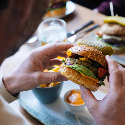 A close up image showing a person sat at a table within the interior restaurant seating area holding a burger at a Heritage venue.