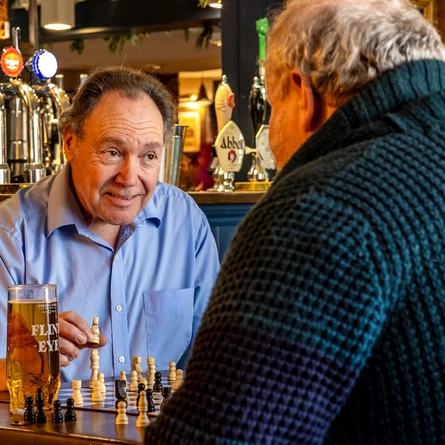 Two men sitting at a table with a pint of Flint Eye playing chess.