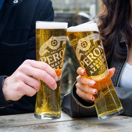 Two people sitting at a table in a beer garden, holding glasses of Peroni beer.