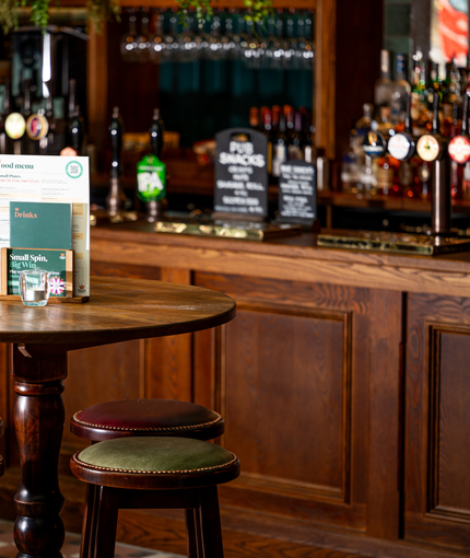 A close up view of a circular, wooden restaurant table with four bar stools, standing in front of the wood panelled bar inside The Junction.