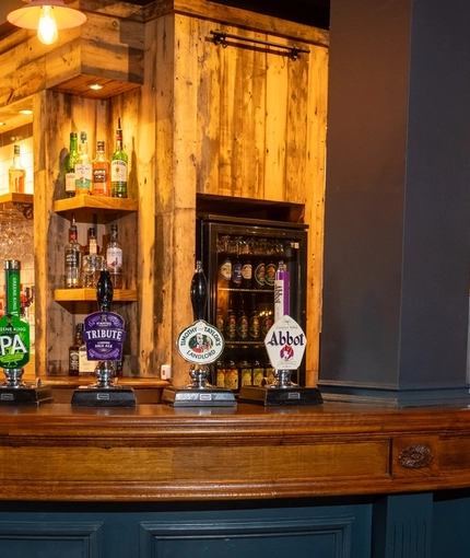 The wood panelled bar inside The Tamar in Crownhill, with glasses hanging in racks above the counter, and bottles of alcoholic spirits on wooden shelves behind the bar.