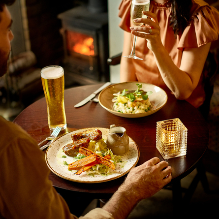An image of 2 customers enjoying 2 mains dishes and various drinks within the interior restaurant seating area at a Chef & Brewer venue.