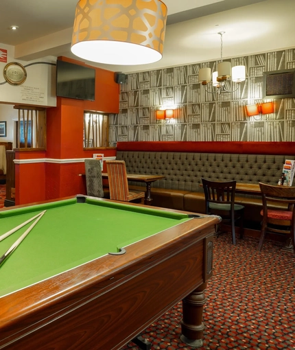 Interior dining area of a pub with a TV, a gambling machine and a pool table.