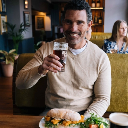 An image focusing on a person sat at a table within the interior restaurant seating area enjoying a drink and a sandwich dish at a Heritage venue.